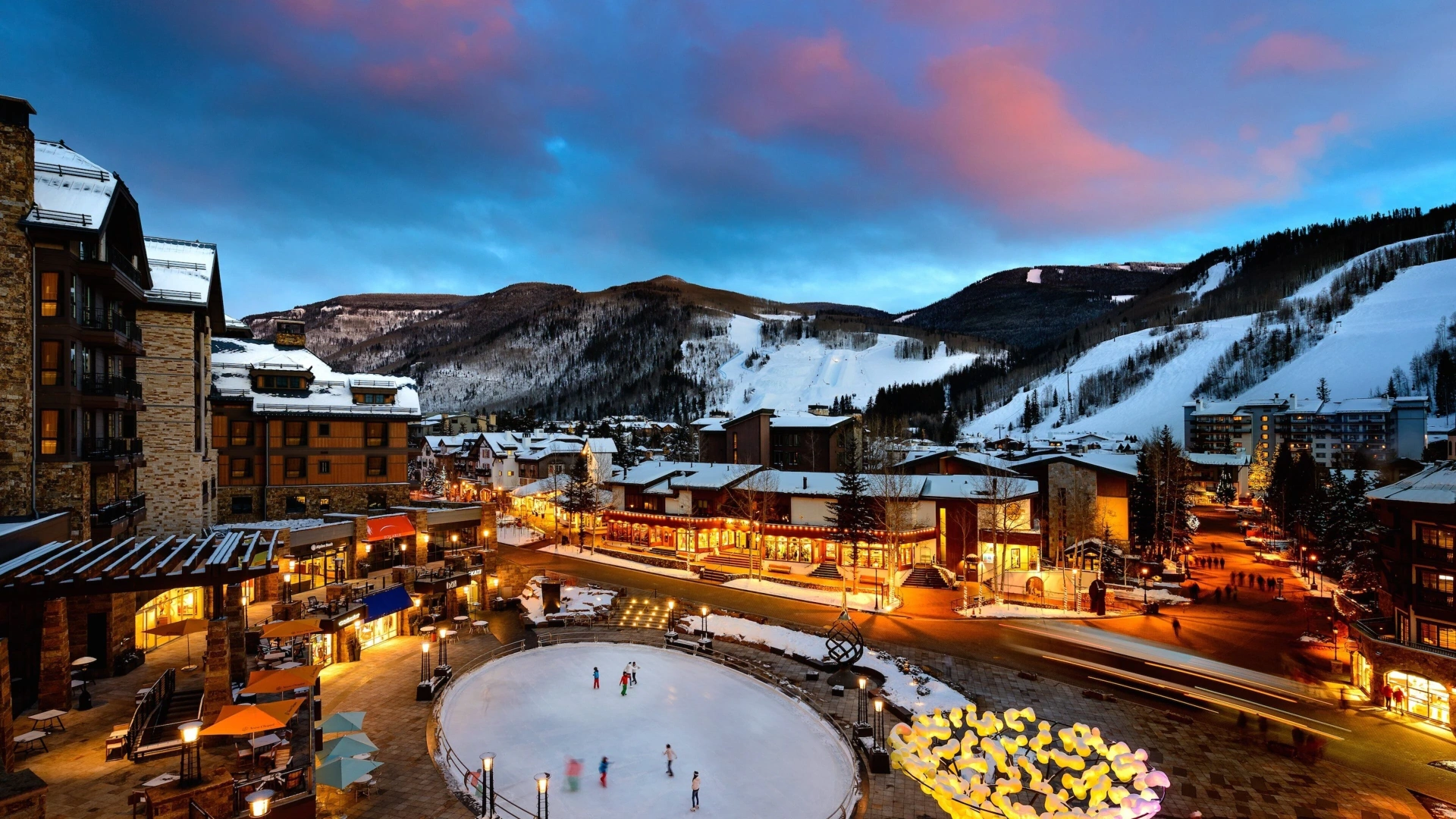 Vail Village at dusk with ice skating rink and snow-covered ski runs above